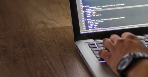 Primer plano de una persona programando en una computadora portátil, mostrando líneas de código de estilos (CSS) sobre un fondo de madera.