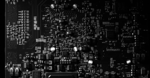 Primer plano de un circuito impreso de color negro con microchips y componentes electrónicos, representando la infraestructura de software.